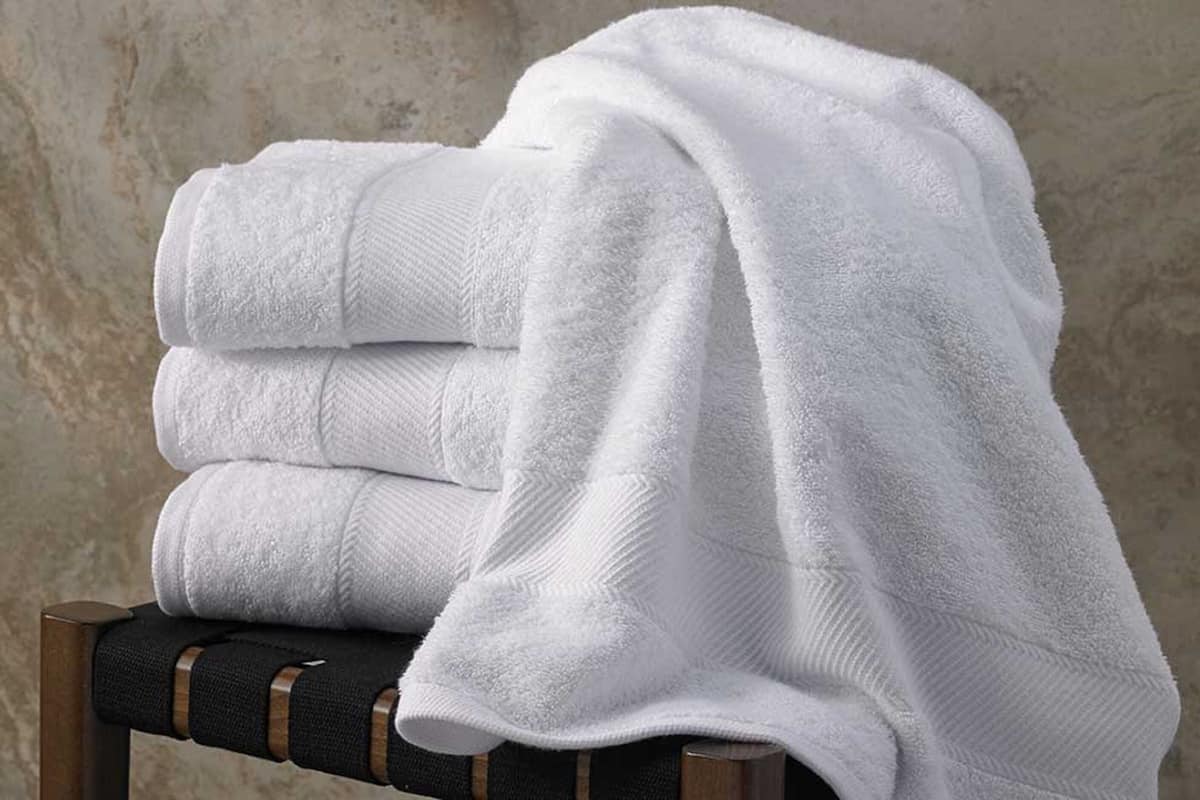 A stack of white towels on a chair with a textured wall in the background.