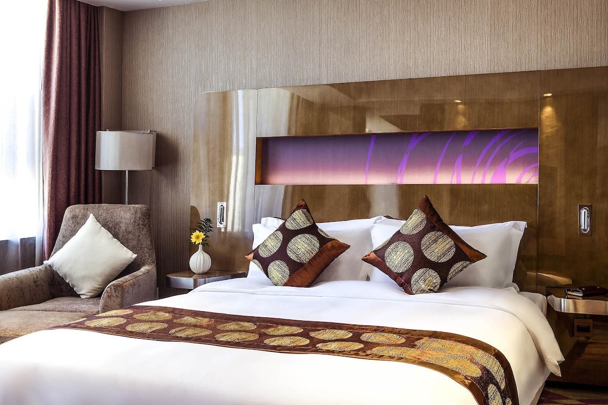 A hotel room with a large bed, a chair, a nightstand, and a wall-mounted lamp.