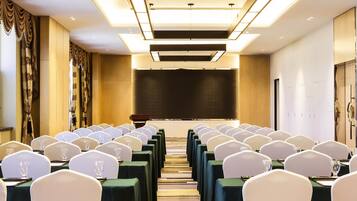 A conference room with rows of tables, chairs, and a large screen at the front.