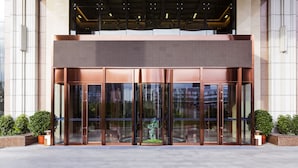 Une entrée moderne avec des portes en verre, une façade de couleur bronze et des plantes en pot.