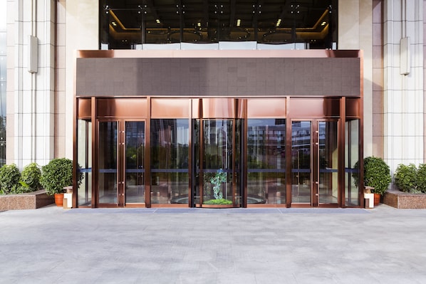 A modern building entrance with glass doors, a bronze-colored facade, and potted plants. - Novotel Daqing Haofang (Daqing)