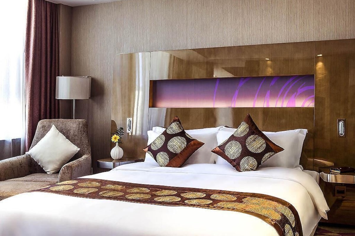 A hotel room with a large bed, a chair, a nightstand, and a wall-mounted TV.
