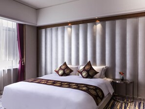A hotel room with a large bed, a headboard with vertical panels, a bedside table with a vase, and a window with sheer curtains. - Novotel Daqing Haofang (Daqing)