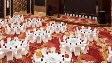 A conference room with multiple round tables, white chairs, and a stage with speakers.