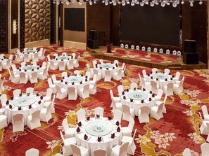 Une salle de conférence équipée de plusieurs tables rondes, de chaises blanches et d’une scène avec un pupitre.