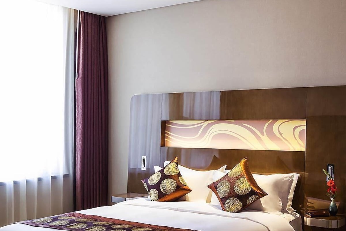 A hotel room with a large bed, two decorative pillows, a nightstand, and a vase with flowers.