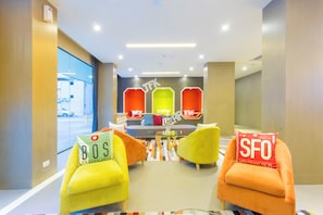 Un área de estar moderna con sillones coloridos, una mesa de centro de vidrio y vista a la calle.