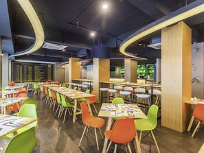 A modern dining area with multiple tables and chairs, a digital arrival board, and a bar area.