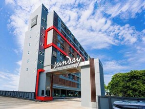 Un hotel de varios pisos con un llamativo letrero de 'Sunday', una fachada moderna y cielo despejado.