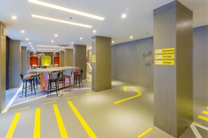 A modern hotel lobby with a reception desk, seating area, directional signs, and a lounge.