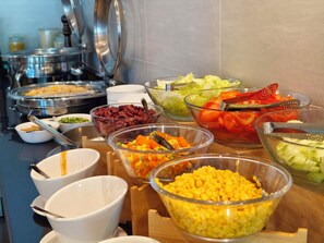Un bufé con diversos alimentos, incluyendo frijoles, verduras y maíz.