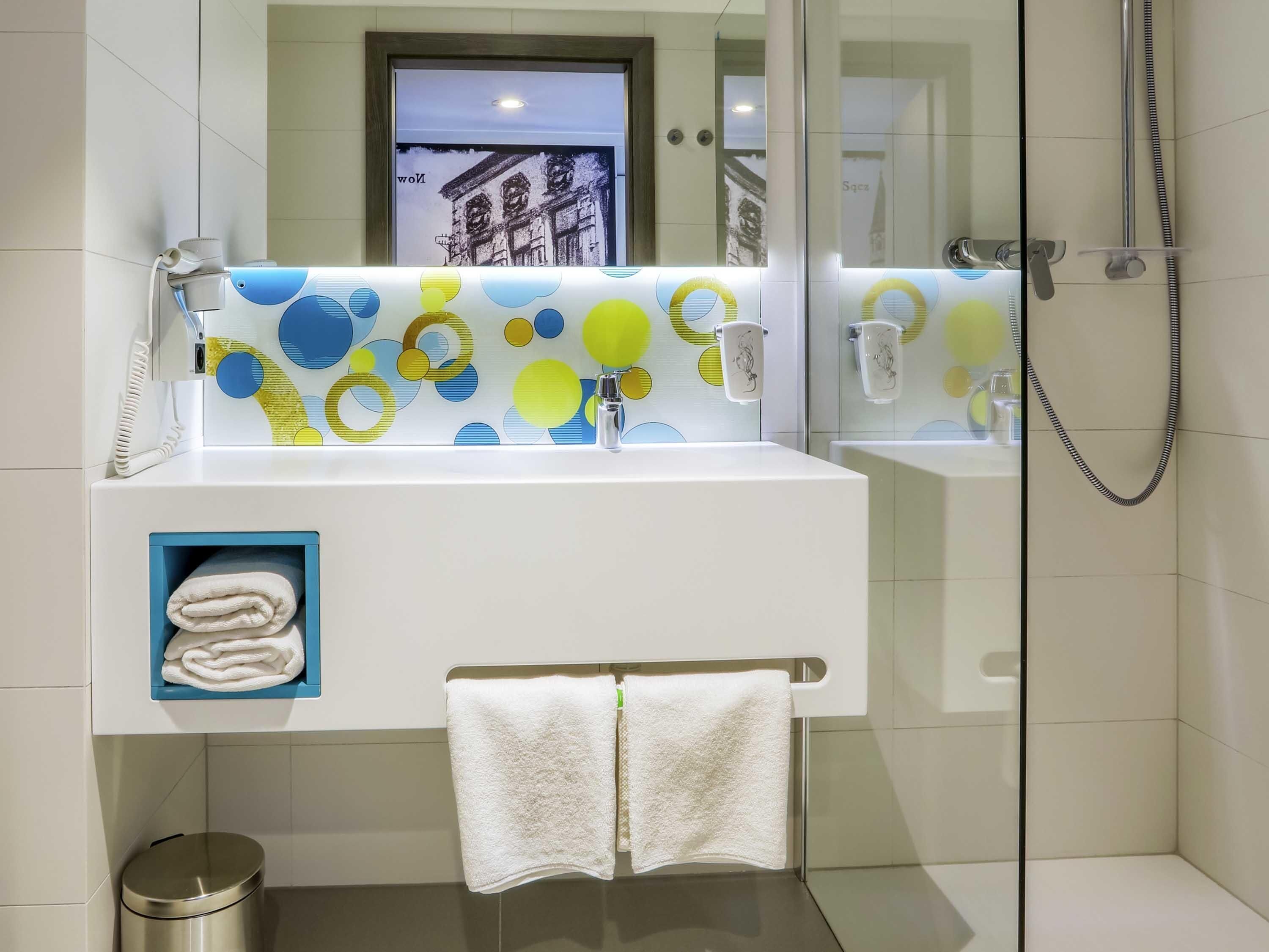 Un baño moderno con un lavamanos blanco, un espejo y una cabina de ducha con mampara de vidrio.
