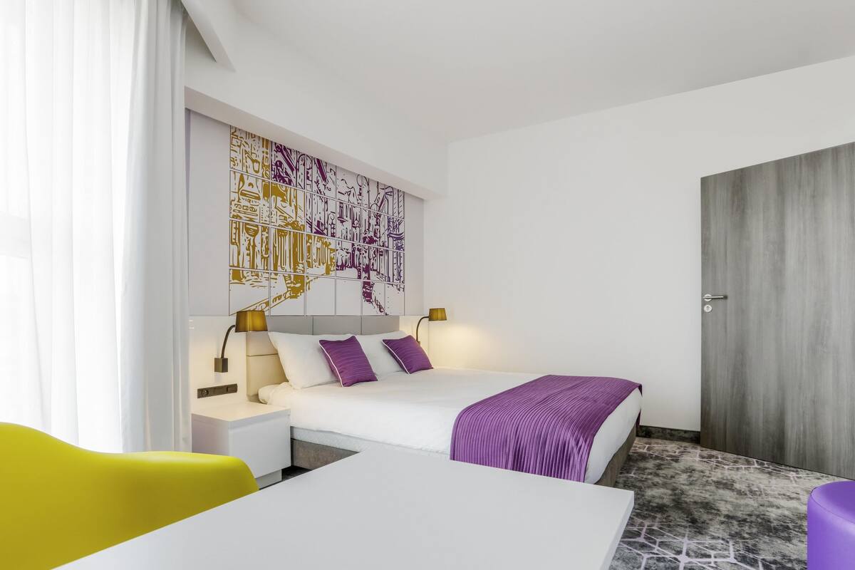 Une chambre d’hôtel moderne équipée d’un lit, de tables de chevet, d’un bureau et d’une chaise.