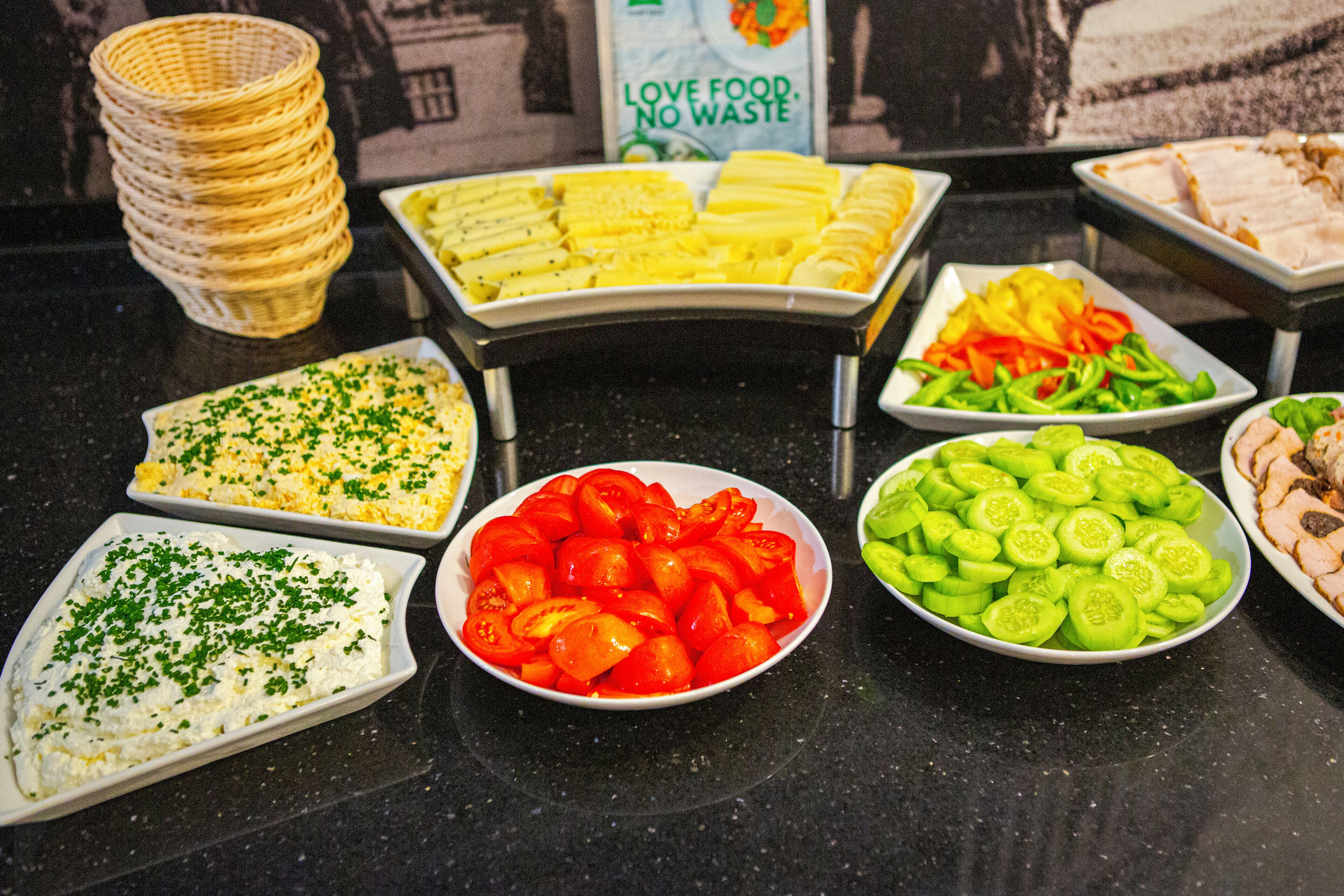 A buffet with various food items including sliced tomatoes, cucumbers, and a dish with a green topping.