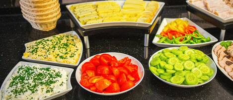 A buffet with various food items including sliced tomatoes, cucumbers, and a dish with a green topping.
