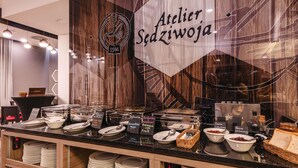 Una barra de buffet con alimentos etiquetados y un letrero que dice 'Atelier Szadzewoja'.