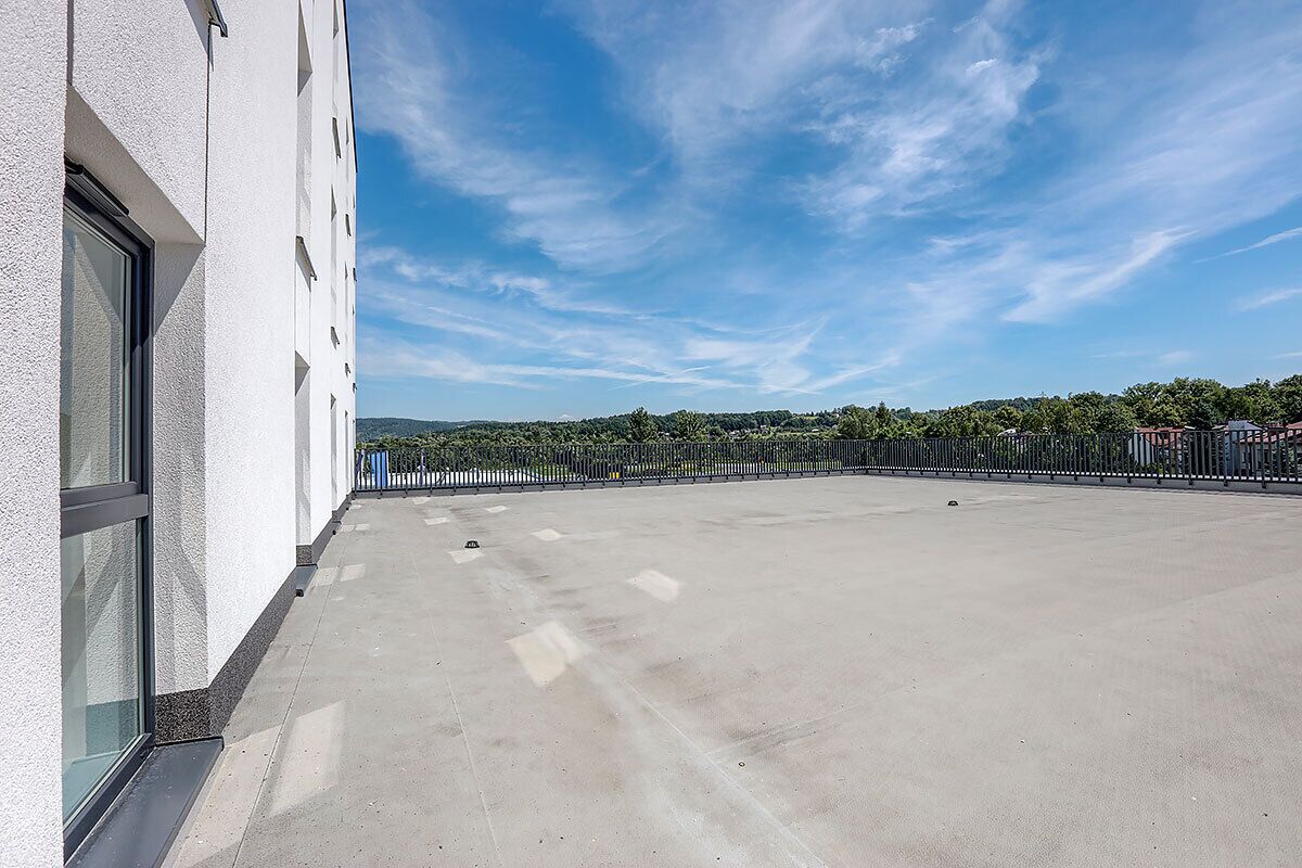 Una terraza en la azotea con vistas despejadas del paisaje circundante, un edificio blanco y una valla de metal.