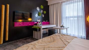 Una habitación de hotel moderna con cama, escritorio, televisión y ventana con cortinas.