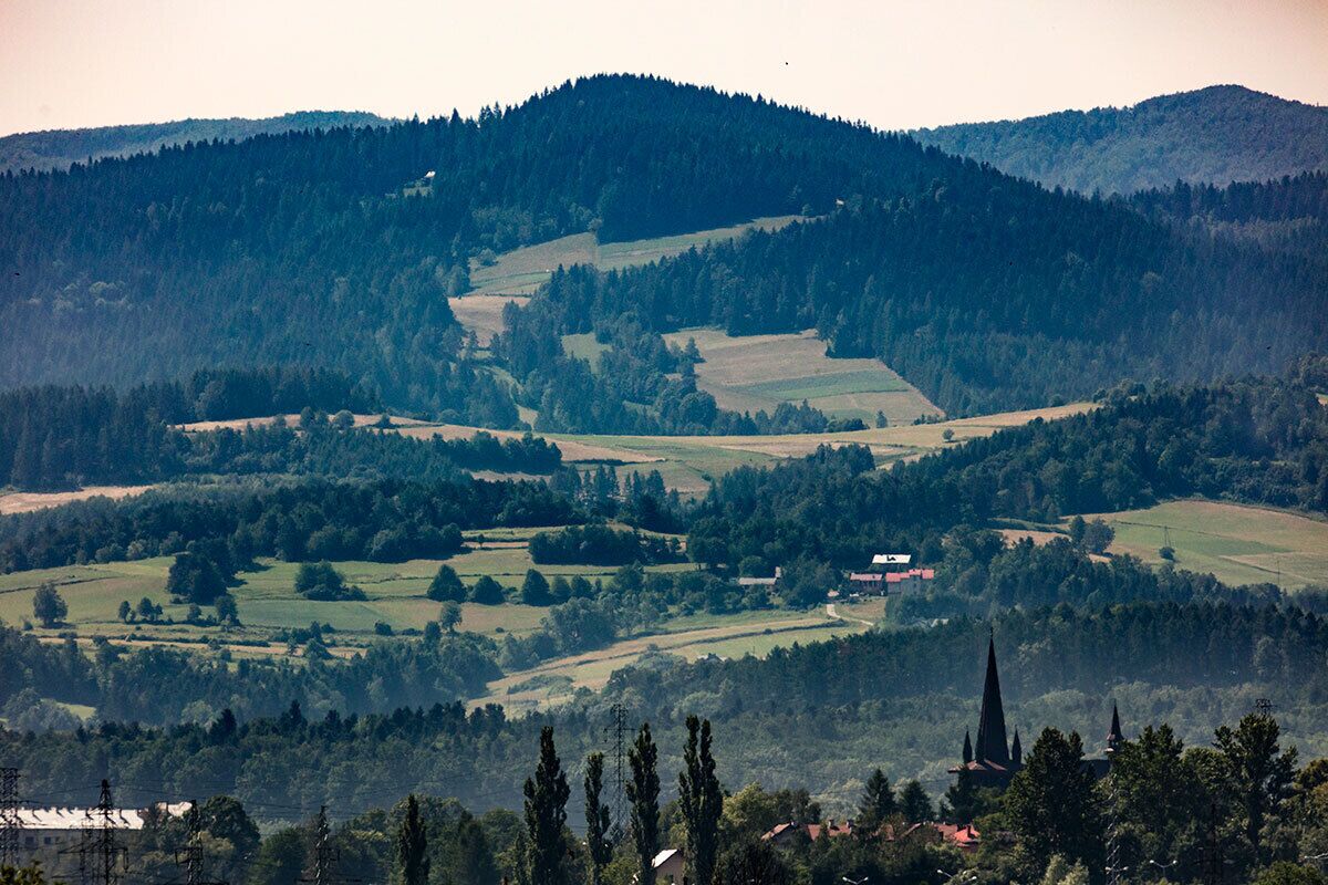 A rural landscape with rolling hills, scattered fields, and a church spire.