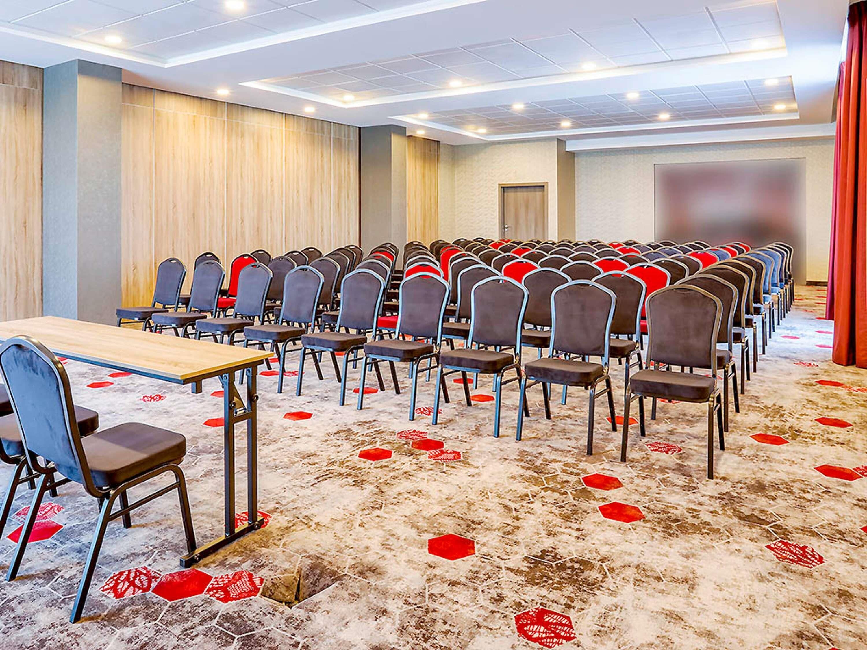 A conference room with rows of chairs, a table, and a carpet with red leaf patterns.