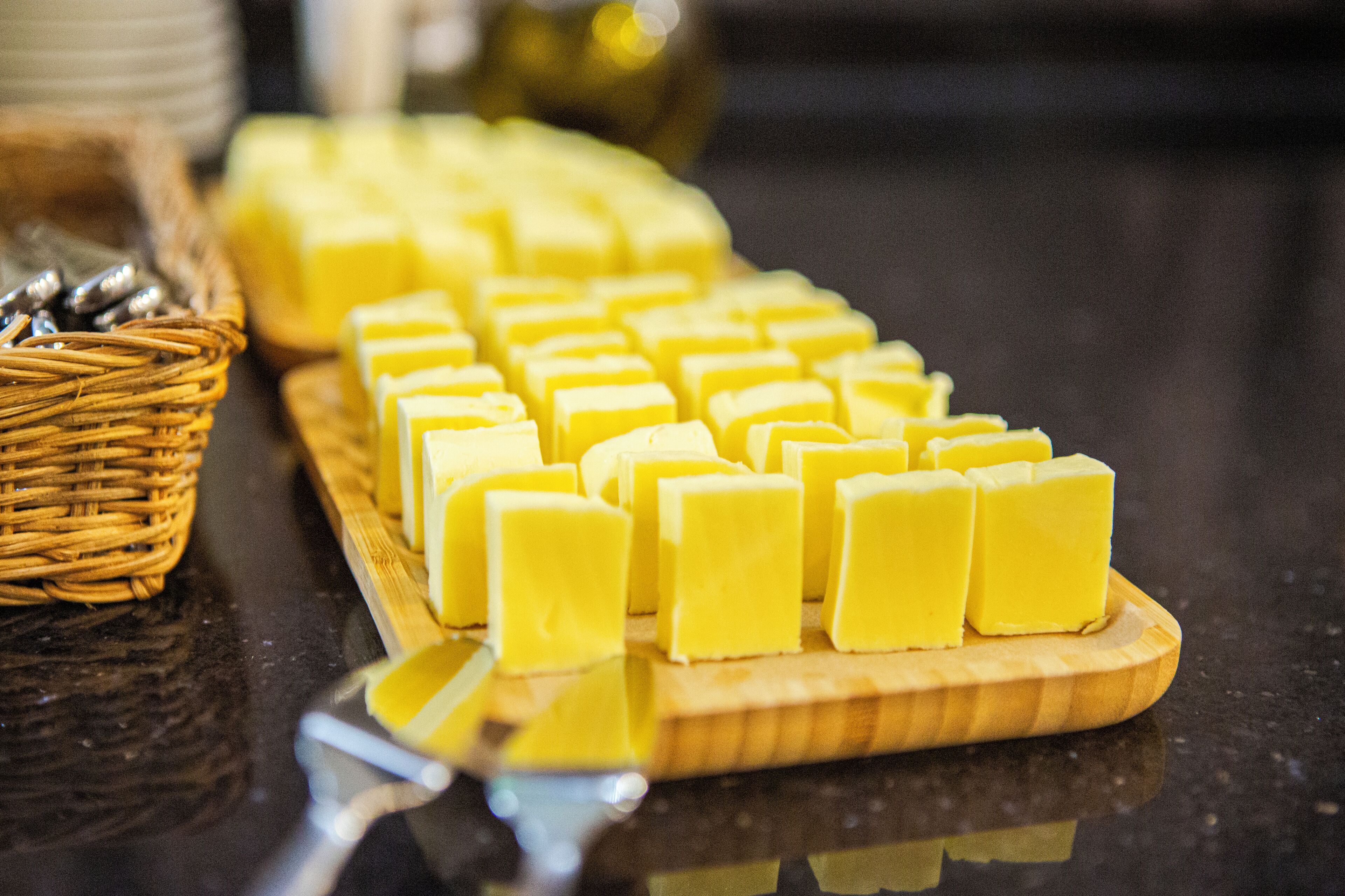 A wooden board with neatly arranged yellow blocks, possibly cheese, on a reflective surface.