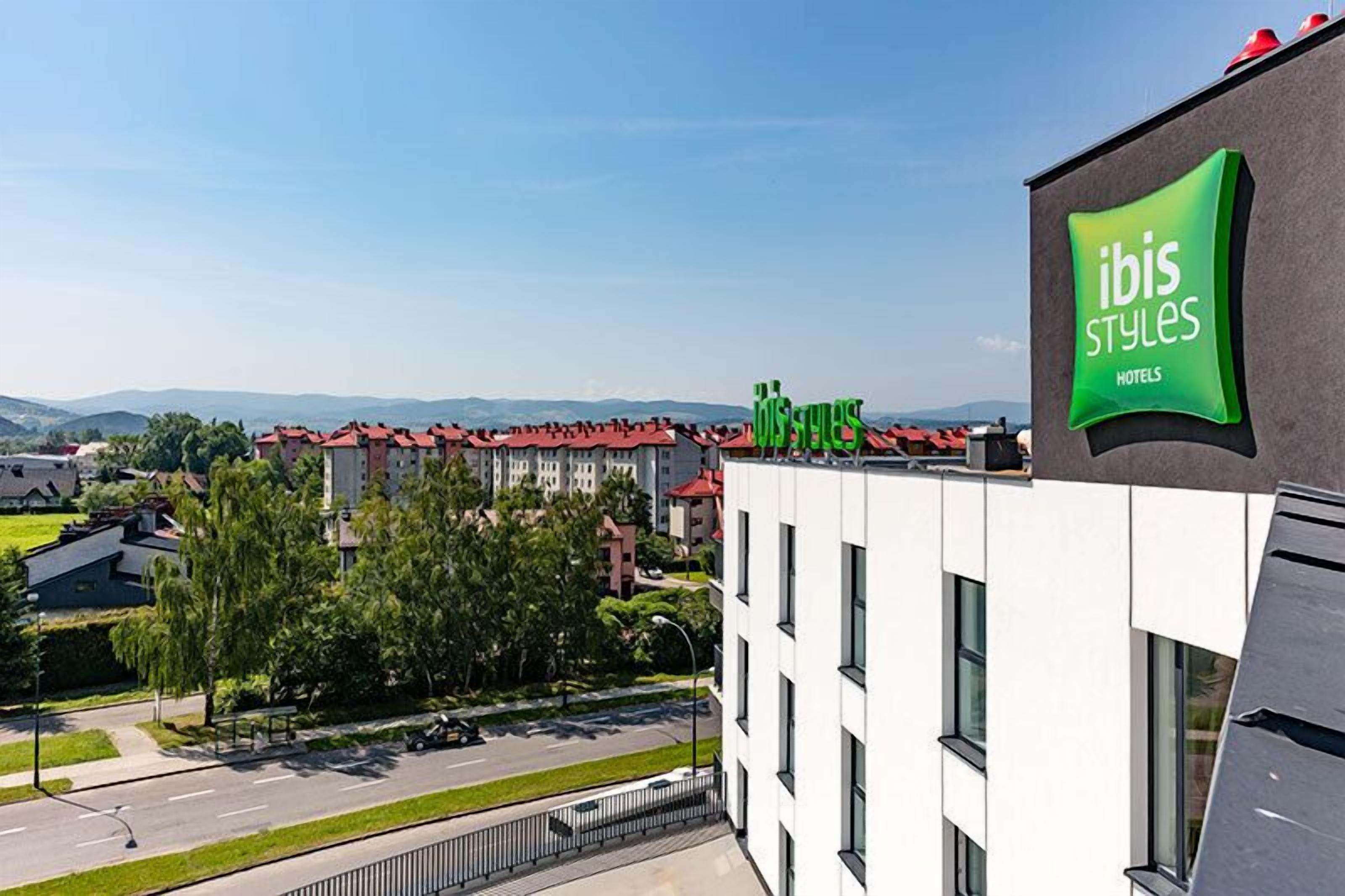 A modern hotel building with a prominent green logo for ibis styles hotels.
