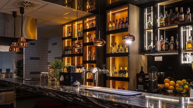 Zona de bar con mostrador de mármol, varias estanterías llenas de botellas de licor y una variedad de utensilios de bar.