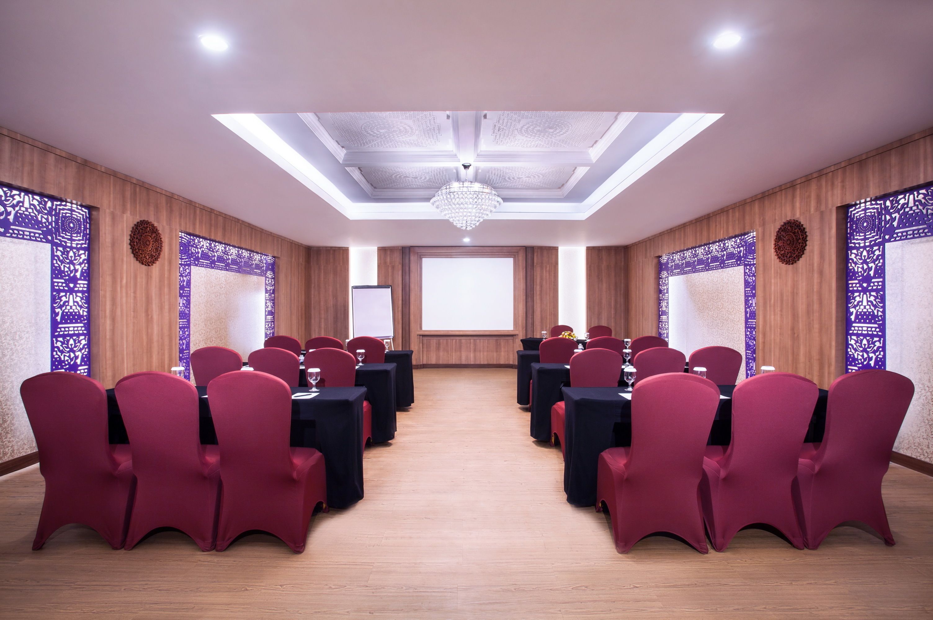 A conference room with red chairs and black tables, a chandelier, and patterned wall panels.