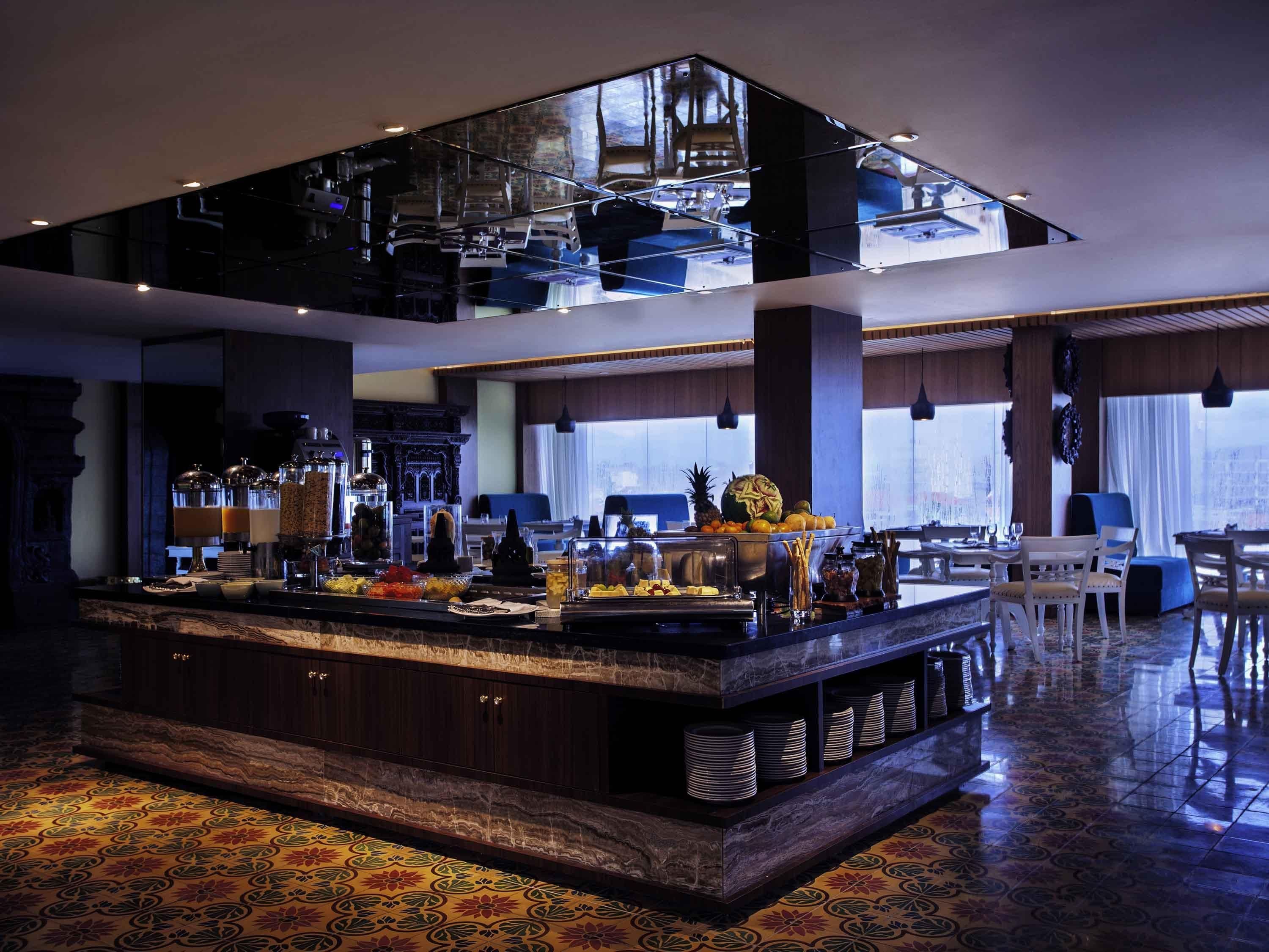 A spacious hotel lobby with a central bar area, seating arrangements, and a large window providing a view.