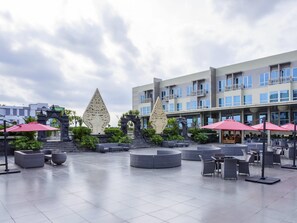 A spacious outdoor area with modern seating and decorative elements, including two large sculptures and a building with balconies in the background. - Grand Mercure Yogyakarta Adi Sucipto (Yogyakarta)