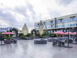 Un vaste espace extérieur doté de mobilier moderne et d’éléments décoratifs, notamment deux grandes sculptures et un bâtiment avec des balcons en arrière-plan.