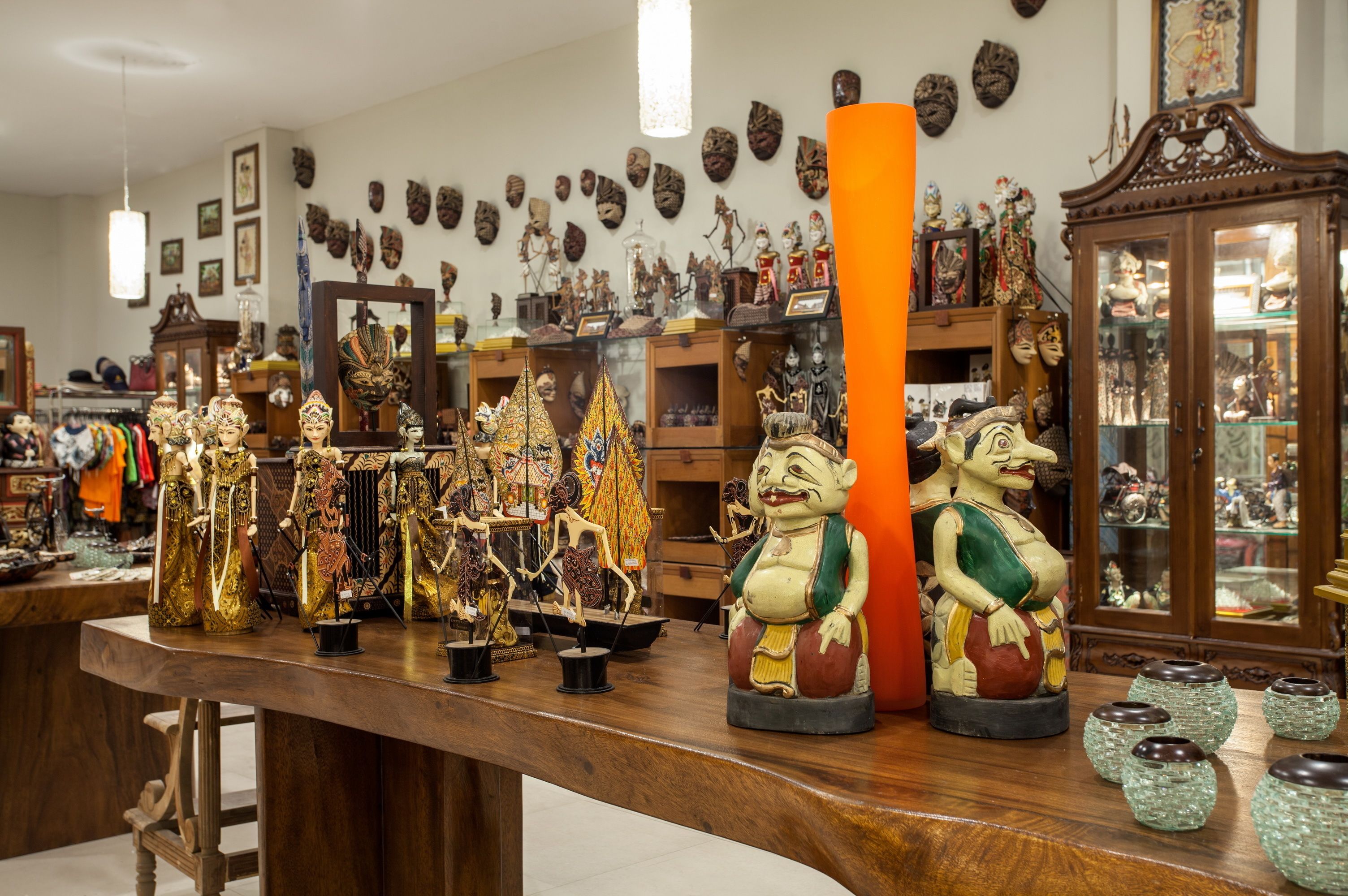 Une pièce meublée de meubles en bois, avec un grand vase orange et divers objets décoratifs disposés sur des étagères.