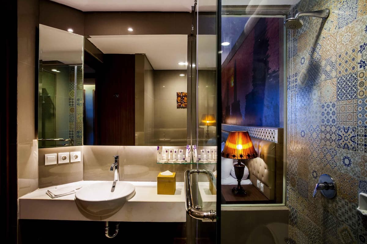 A modern bathroom with a glass shower enclosure, a large mirror, a white sink, and a patterned tile wall.
