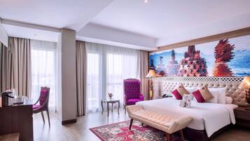 A hotel room with a bed, a desk, a chair, a small table, and a large window.