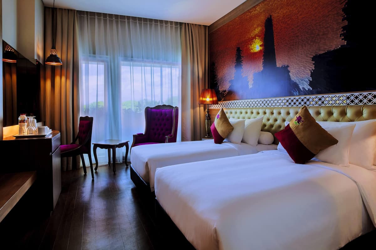 A hotel room with two beds, a desk with a chair, a table with a water bottle, and a large window with curtains.