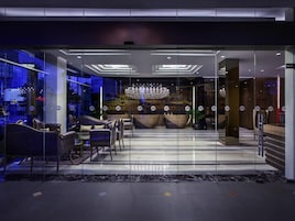 A modern hotel lobby with a glass entrance, seating area, and a chandelier.