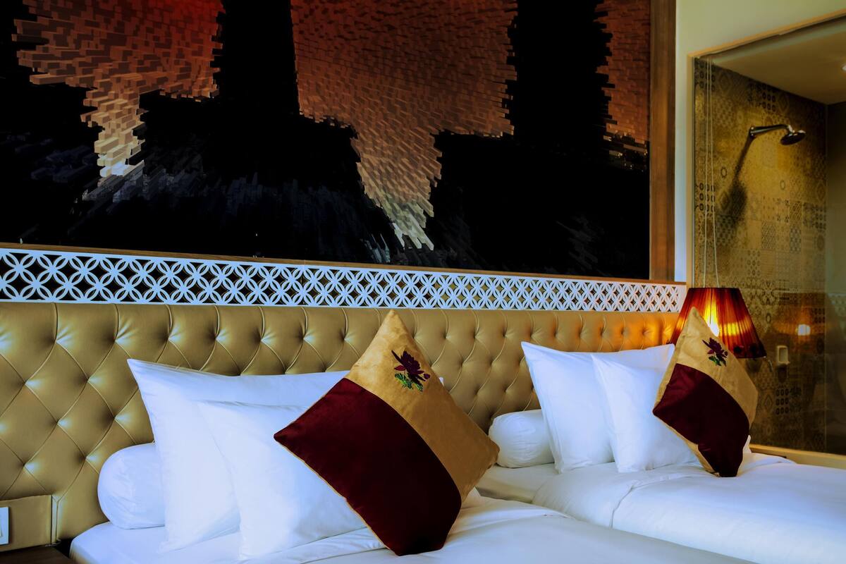 A hotel room with a tufted headboard, white bedding, and a decorative wall with a geometric pattern.