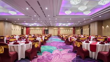 A banquet hall with round tables, red and gold chairs, and chandeliers.