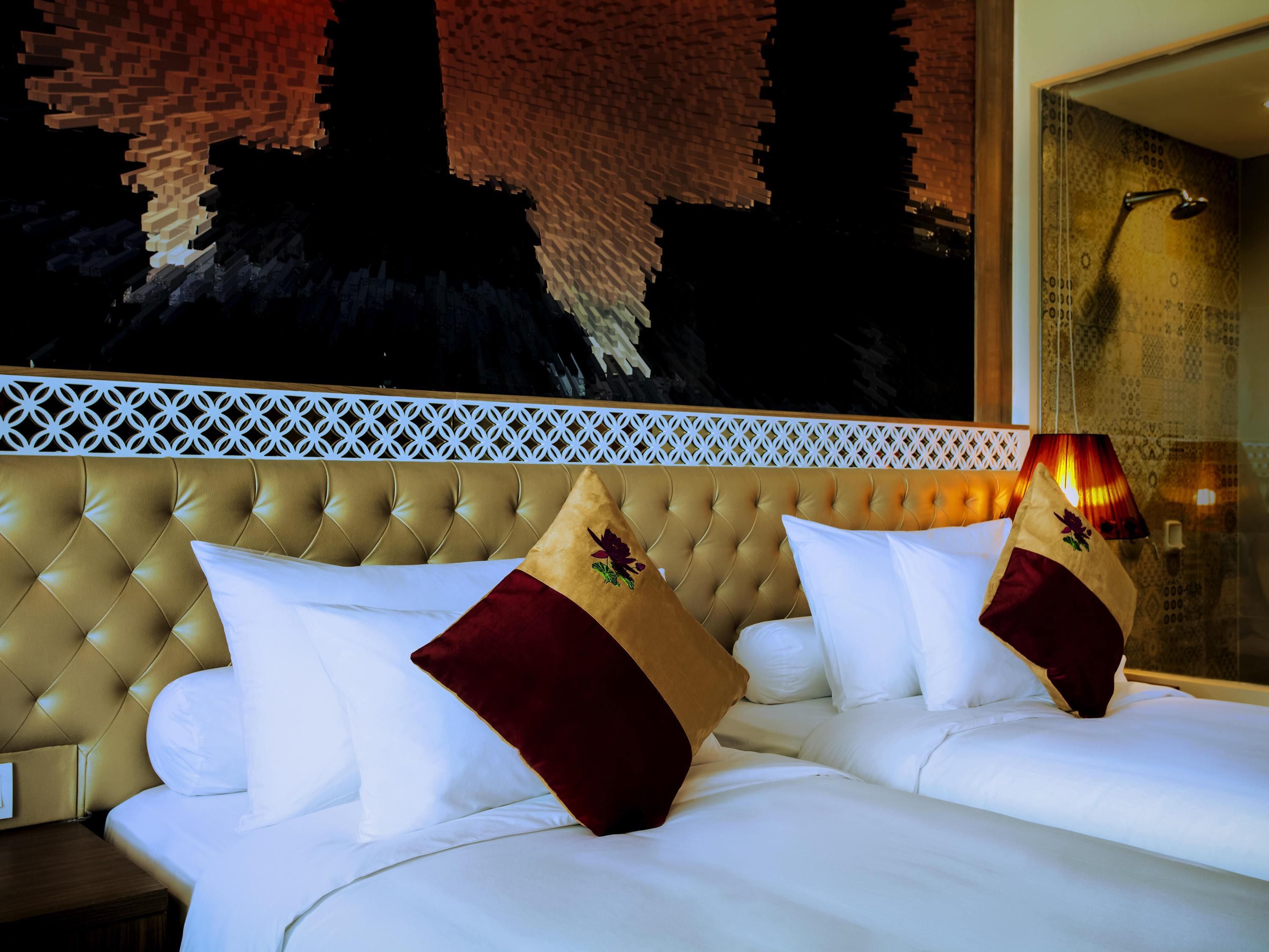 Een hotelkamer met een gestoffeerd hoofdeinde, witte beddengoed en een decoratieve muur met een geometrisch patroon.
