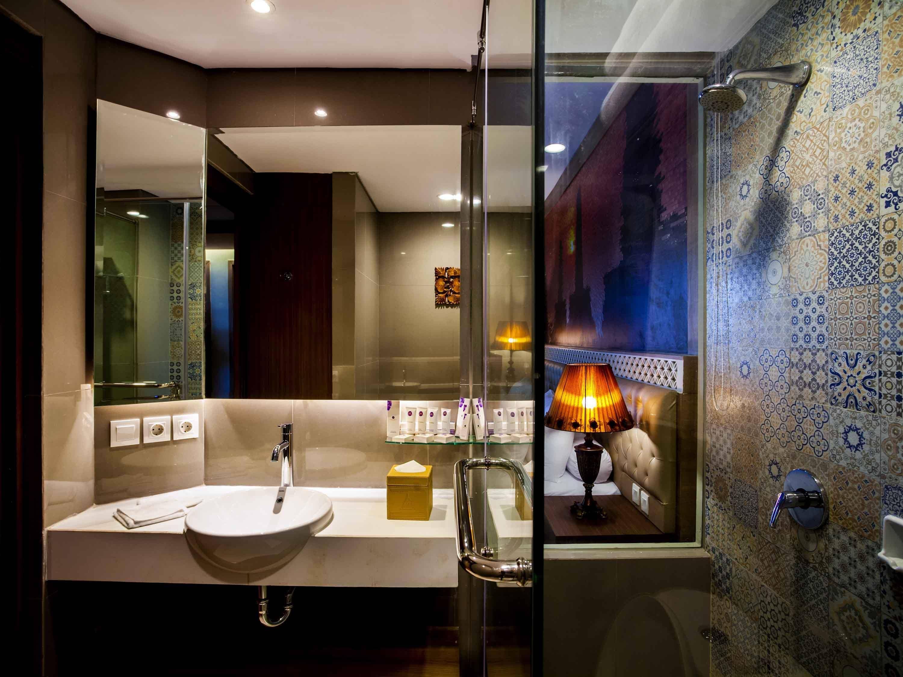 A modern bathroom with a glass shower enclosure, a large mirror, a white sink, and a patterned tile wall.
