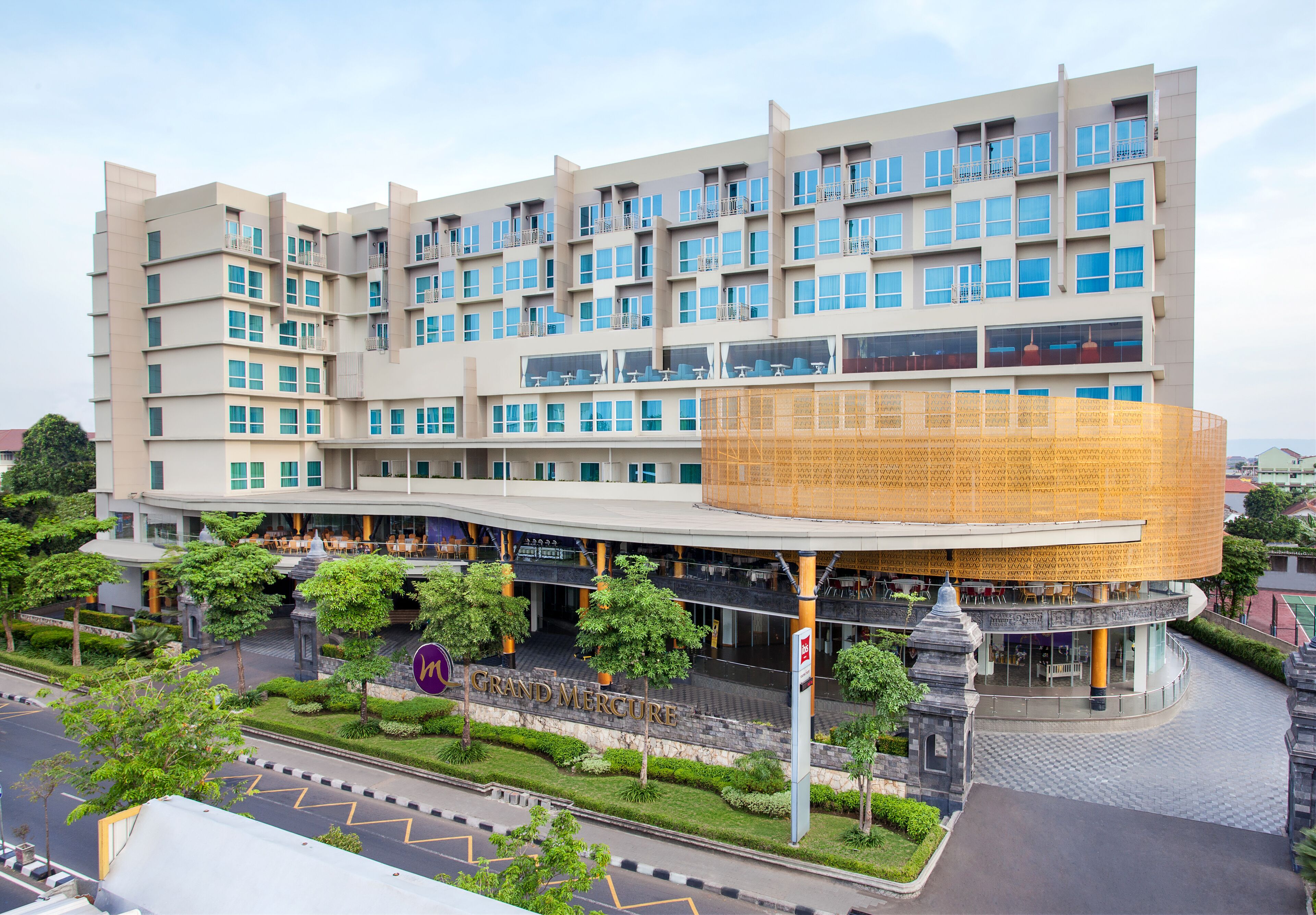 A multi-story hotel with a distinctive circular atrium and a well-maintained garden area.