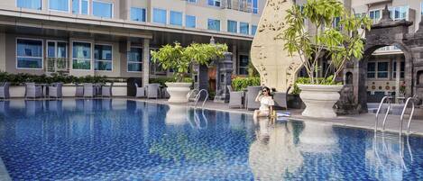 A swimming pool with a tiled floor, surrounded by lounge chairs and potted plants.