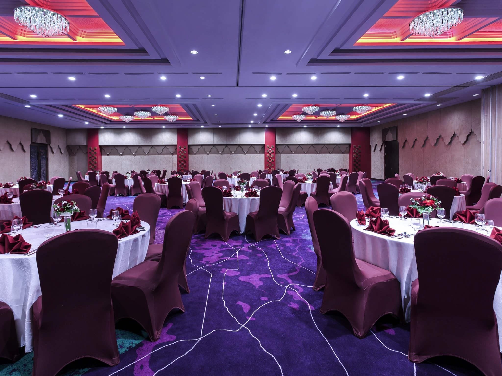 Une salle de banquet avec des tables rondes, des chaises rouges et des lustres.