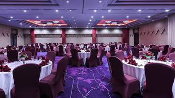 Une salle de banquet avec des tables rondes, des chaises rouges et des lustres.