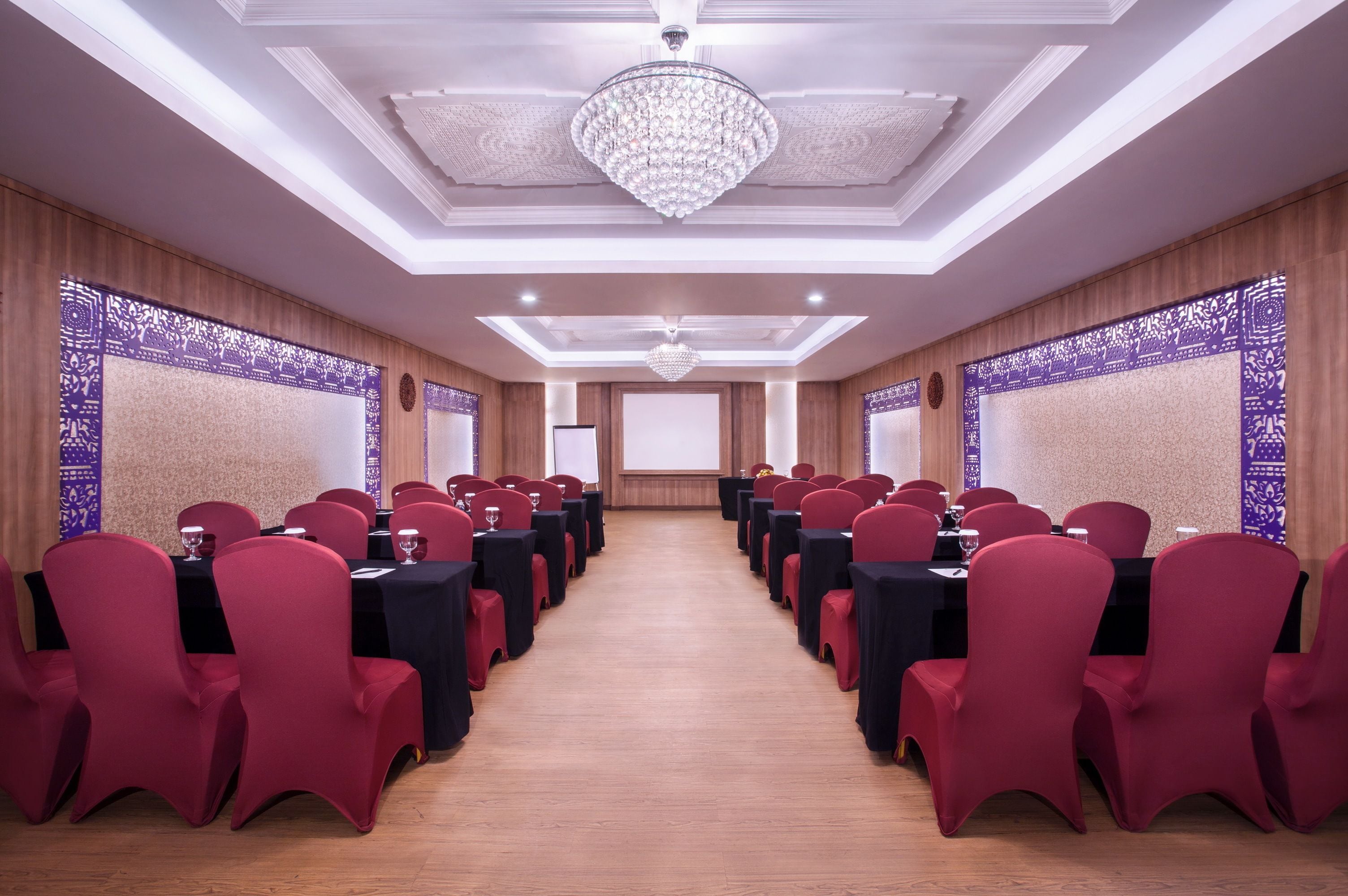 A conference room with rows of red chairs and black tables, a chandelier, and patterned wall panels.