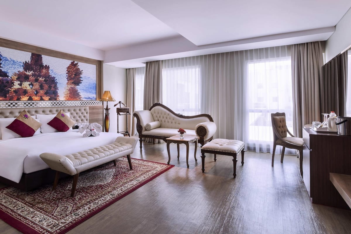 A hotel room with a bed, a sofa, a chair, a small table, and a painting on the wall.