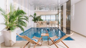 Un área de piscina interior moderna con techo de vidrio, sillones de mimbre y una mesa de comedor.