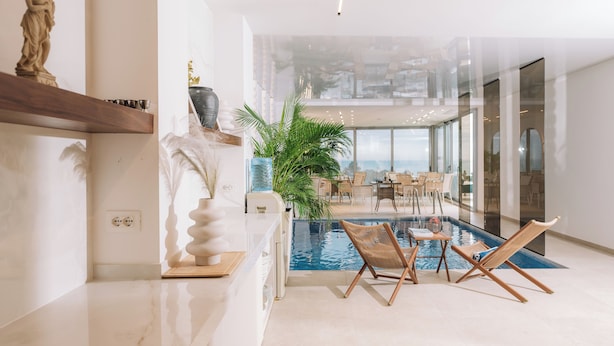 Un área de piscina interior moderna con sillones de descanso, una estatua en un estante y un amplio ventanal con vistas a la piscina.