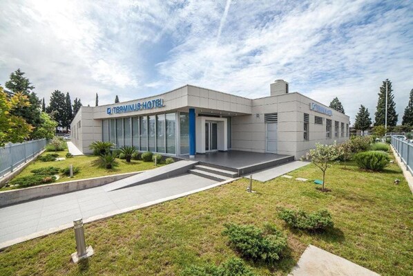 A modern hotel with a flat facade, large windows, and a well-maintained lawn. - Hotel Terminus (Podgorica)