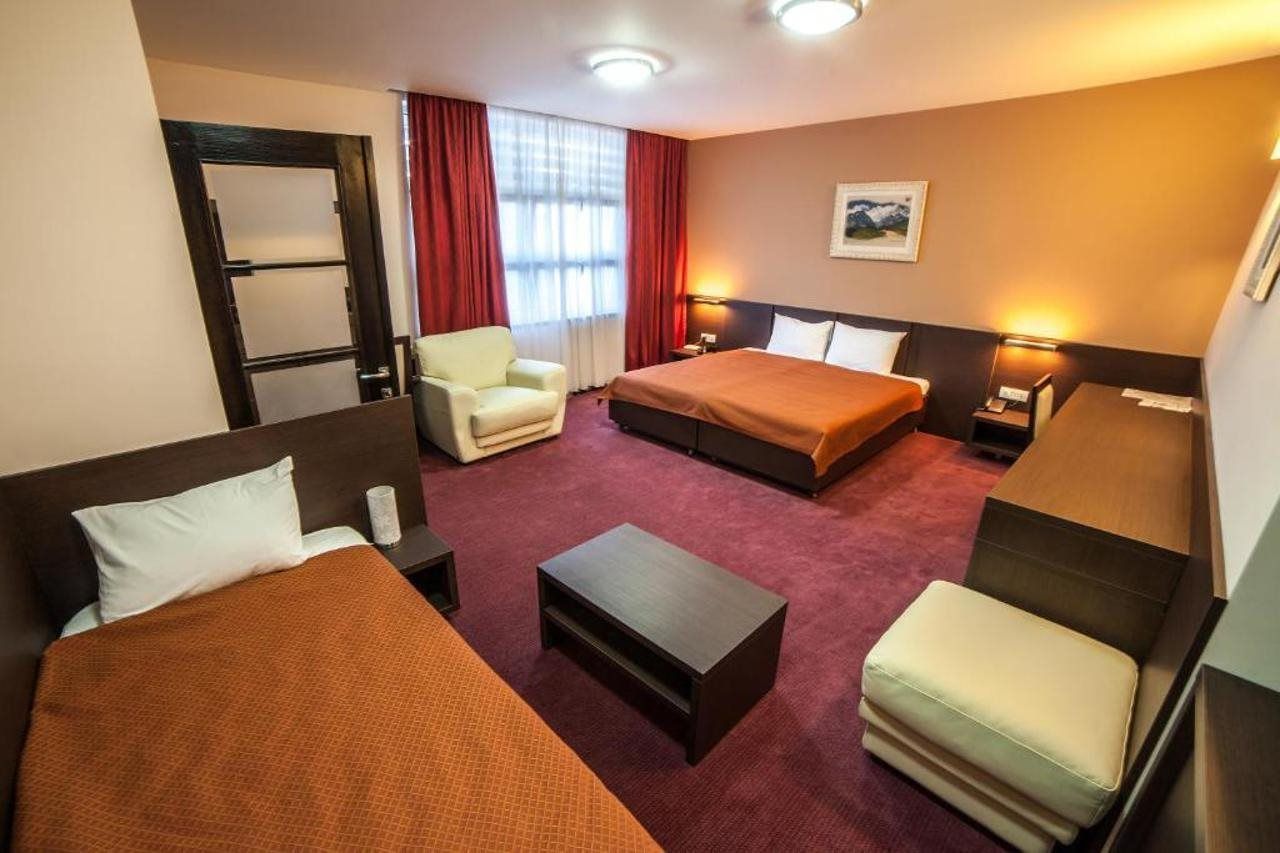A hotel room with two beds, a desk, a chair, and a small table.